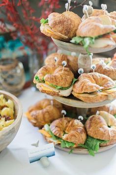 sandwiches and croissants are arranged on three tiered trays for display