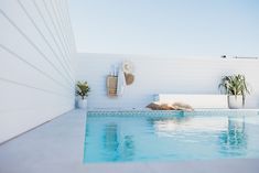 a swimming pool with plants and towels on the wall next to it, in front of a white building