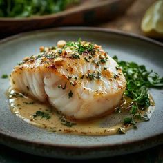 a piece of fish on a plate covered in sauce and garnished with parsley