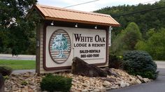 the sign for white oak lodge and resort is surrounded by rocks, shrubs, and trees