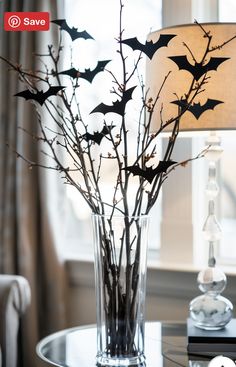 a glass vase filled with branches and bats on top of a table next to a lamp