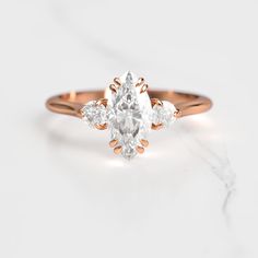 an oval cut diamond ring with three pear shaped diamonds on the band, set in 18k rose gold