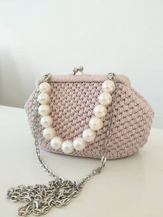 a pink purse with pearls hanging from it's chain on a white counter top