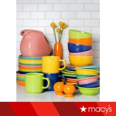 a stack of colorful dishes and cups on top of a white counter next to a brick wall