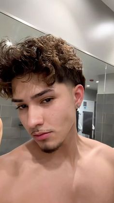 a shirtless young man brushing his hair in front of a mirror with the reflection of another person taking a selfie