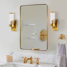 a bathroom sink with two gold faucets and a large square mirror above it