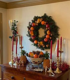 a table topped with fruit and candles next to a wreath on top of a dresser