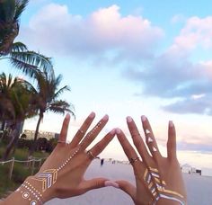 two hands with tattoos on their fingers and palm trees in the background