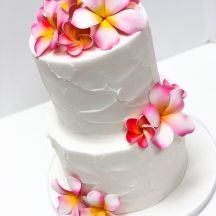 a three tiered white cake with pink and yellow flowers on the top, sitting on a plate