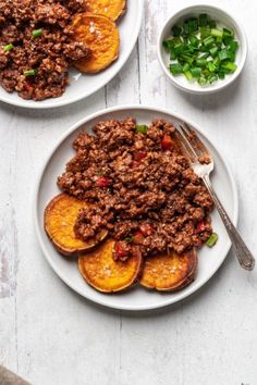 two plates filled with meat and vegetables on top of a white table next to bowls