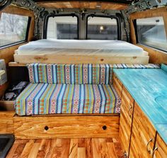 the interior of an old camper van with wood flooring and colorful cushions on it