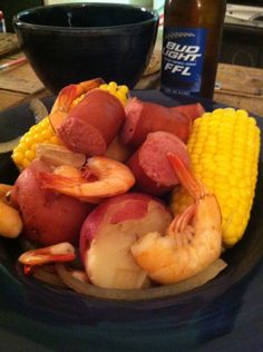 a plate full of shrimp, potatoes and corn on the cob next to a beer