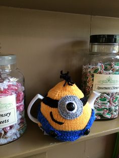 there is a knitted tea pot with a smiley face on it and candy in the background