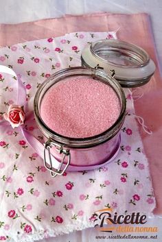 pink glitter in a jar sitting on top of a flowery cloth next to a spoon