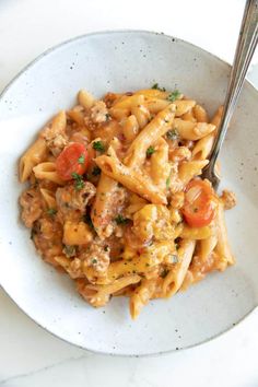 a white bowl filled with pasta covered in meat and tomato sauce next to a fork