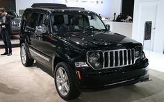 a man standing next to a black jeep on display at an auto show with people looking at it