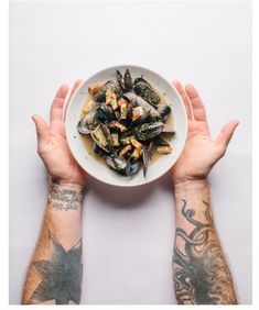 two hands holding a bowl of steamed mussels