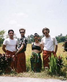 three men and two women standing in front of some tall grass with trees in the background