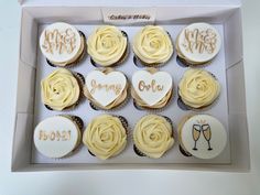 twelve cupcakes in a box with white frosting and gold lettering on them