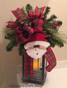 a lantern with a santa clause on it and pine branches in the corner, next to a candle