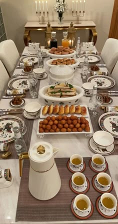 a long table is set with plates, cups and bowls full of food on it