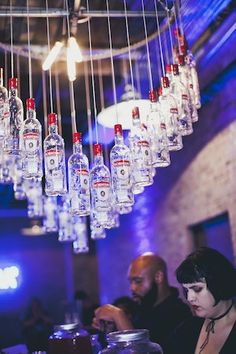 a woman sitting at a bar with lots of bottles hanging from the ceiling