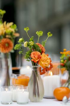 an arrangement of flowers and candles sit on a table in front of other vases