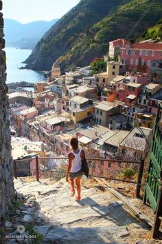 a woman is walking up some steps towards the ocean and houses on the hill behind her