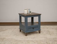 a blue end table with two drawers on the bottom and one drawer open, sitting on a rug in front of a white wall