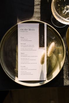 a plate with a menu on it sitting next to a wine glass and silverware