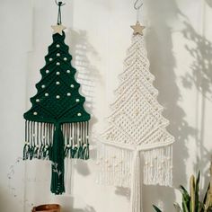 two crocheted christmas trees hanging from hooks on a wall next to a potted plant