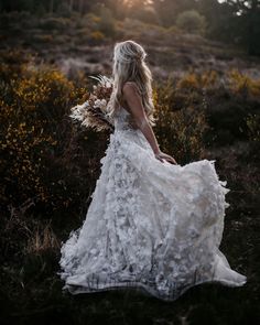 a woman in a white dress is walking through the grass with flowers on her back