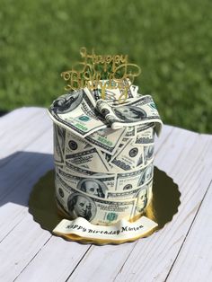 a birthday cake made out of money on top of a wooden table with grass in the background