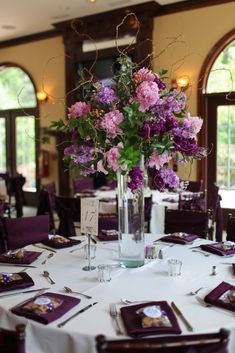 a vase filled with purple flowers sitting on top of a white table cloth covered table