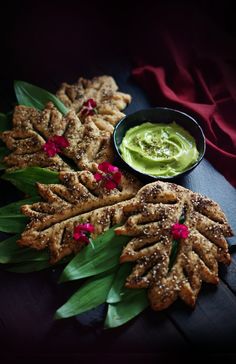 some food is laying out on a table with green sauce in the middle and red flowers around it