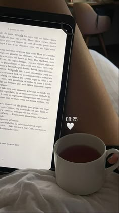 a woman laying in bed next to a cup of tea and an open laptop computer