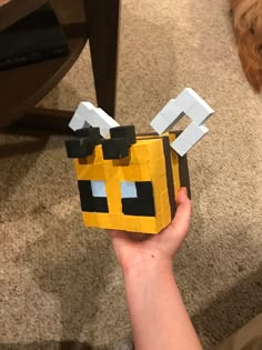 a hand holding up a small yellow box with black eyes and nose on it's face