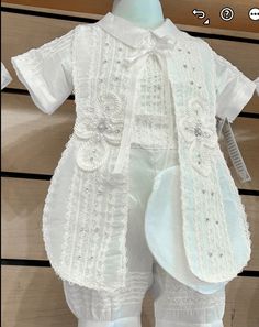 a white shirt and pants are on display in front of a wooden background with an image of a baby's christ gown