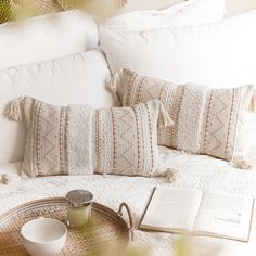 an open book on a tray next to two pillows and a cup sitting on a bed