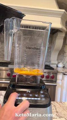 a hand is pressing the button on a blender that has an orange in it