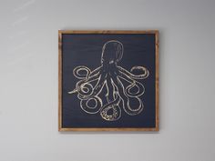 an octopus drawn in gold on a dark blue background hangs above a white painted wall