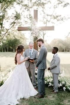 a bride and groom standing in front of a cross during their wedding ceremony at the farm