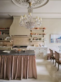 a chandelier hangs from the ceiling in a kitchen with white cabinets and checkered table cloth