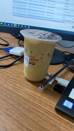 a cup of coffee sitting on top of a wooden desk next to a computer monitor