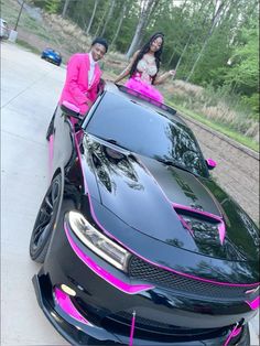 a man and woman sitting on the hood of a black car with pink trims