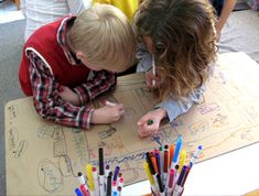 two children are drawing on a piece of paper