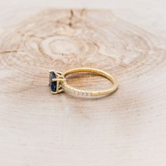 a gold ring with a blue stone and diamond accents on top of a piece of wood