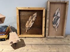 two wooden framed art pieces sitting next to each other on a wood table with books