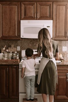 a woman standing next to a little boy in a kitchen near a stove top oven