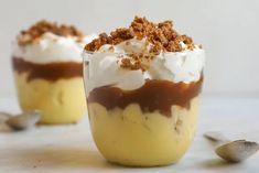 two desserts with whipped cream and toppings in glasses on a white countertop